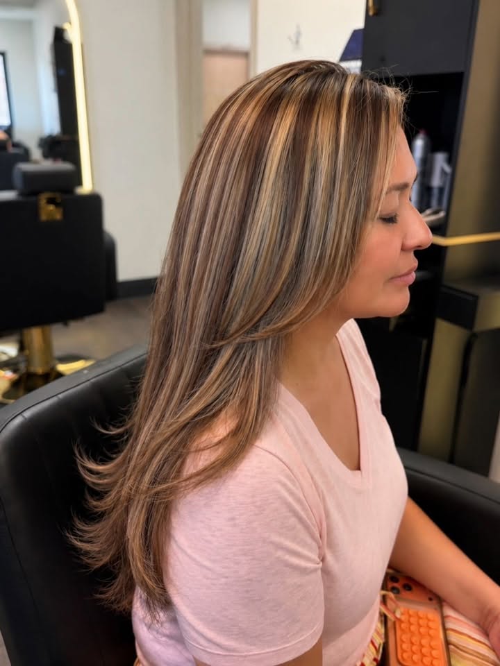 Side profile of client with long layered hair featuring caramel and honey blonde highlights